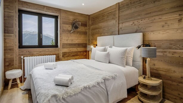 A bedroom with a wooden wall, a large window, a bed with white linens, and a bedside table with a lamp. - Family duplex near Courchevel slopes with wifi and parking (Courchevel 1650)