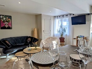 Una sala de estar con un sofá de cuero negro, una mesa de centro redonda de madera, un sillón blanco y una mesa de comedor con platos, vasos y cubiertos.