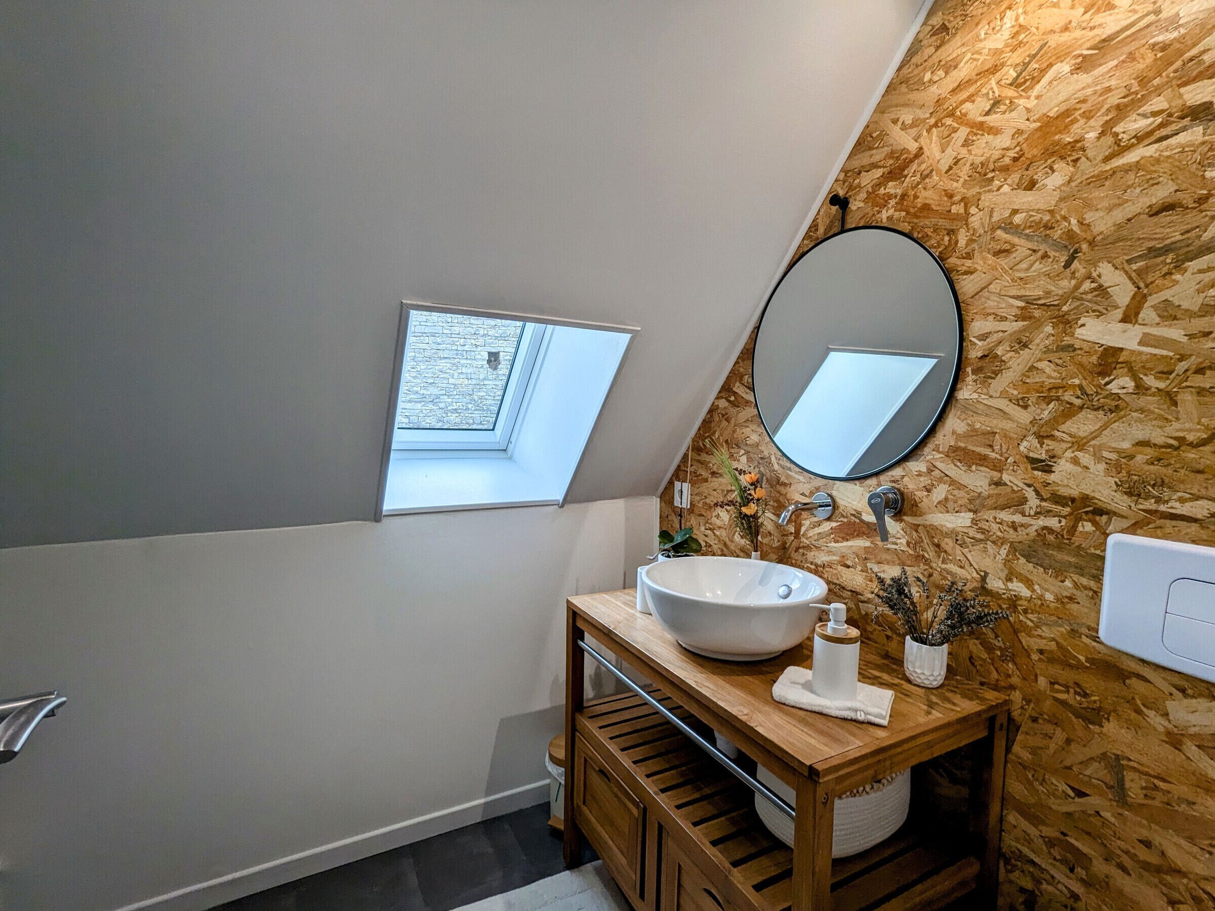 A modern bathroom with a skylight, a round mirror, and a wooden vanity.