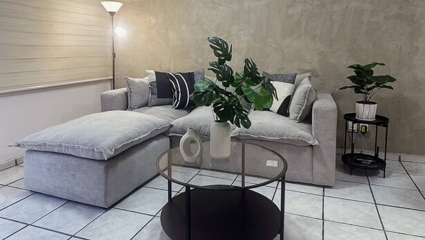 Una sala de estar moderna con un sofá seccional gris, una mesa de centro de vidrio y dos plantas en macetas.