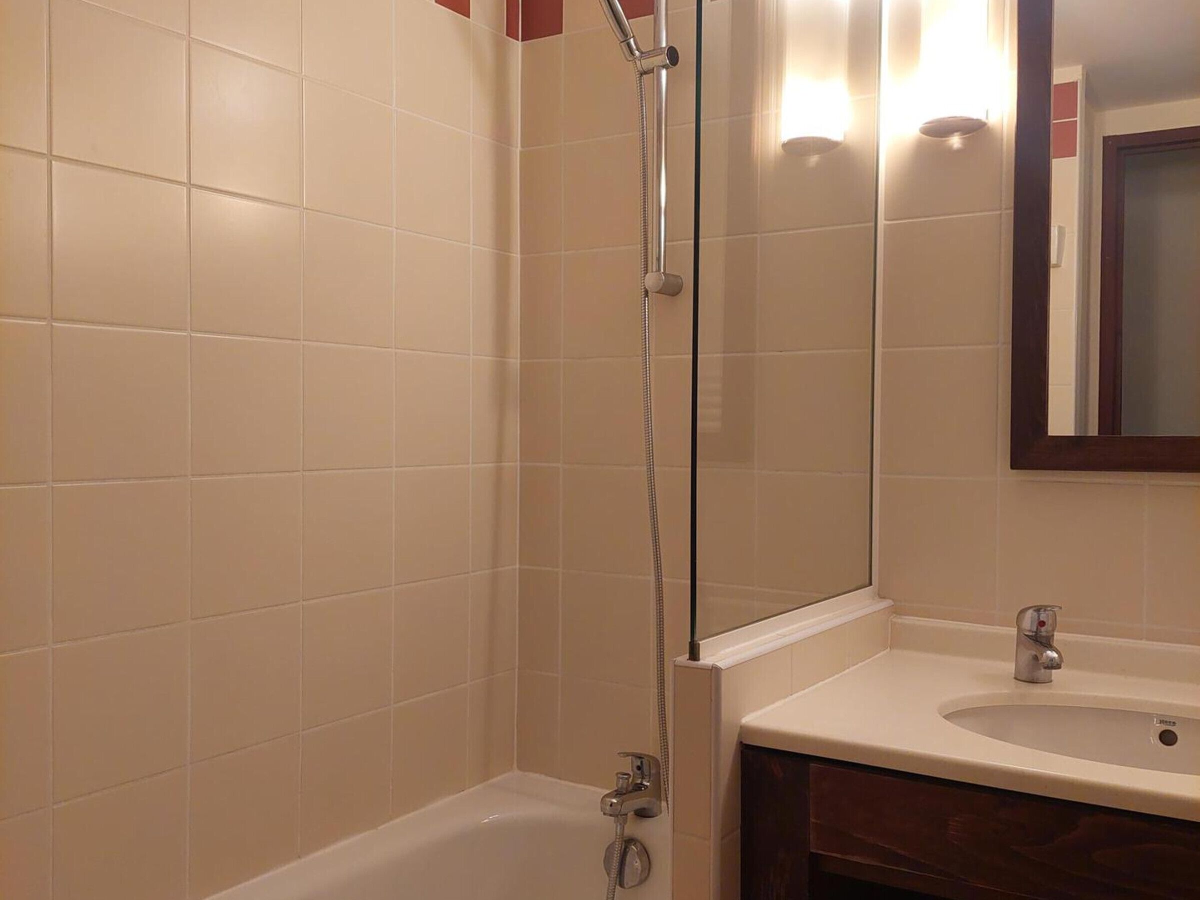 Ein Badezimmer mit beigen Fliesen, einer Glasdusche, einer weißen Badewanne und einem Waschbecken mit Spiegel darüber.