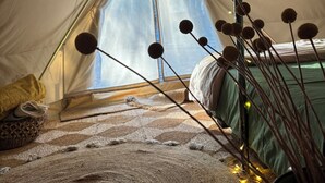 Interior acogedor de una tienda de campaña con una cama, una decoración colgante y vista a árboles por una ventana.