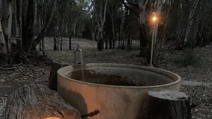 Un hogar de fuego de concreto rodeado de rocas y un tocón de madera, con una vela encendida cerca.