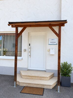 A white door with a wooden pergola entrance, a sign indicating 'JUPAS Saartal Suite,' and a small potted plant beside the steps. - JUPAS° Saartal Suite – Quiet, Playground & Parking (Konz)
