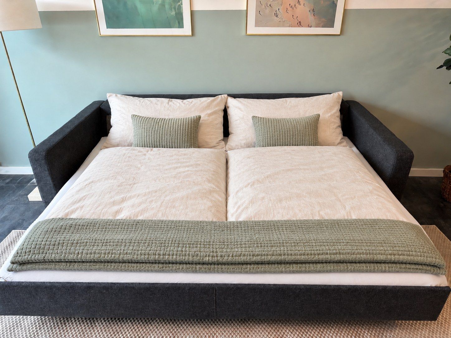 A double bed with a dark headboard, two pillows, and a green throw blanket.