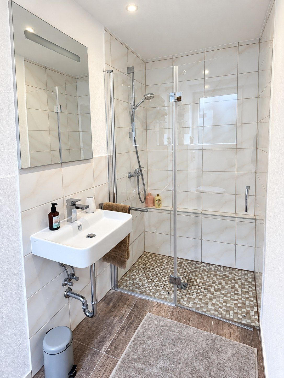 Un baño moderno con ducha acristalada, un lavabo blanco y un espejo sobre él.