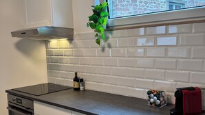 A modern kitchen with white cabinetry, a black countertop, a built-in oven, and a window overlooking a brick building. - JUPAS° | Saartal Suite - Smart & Netflix (Konz)