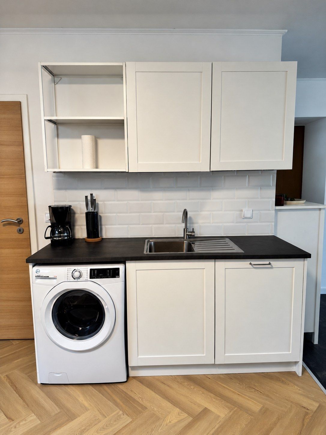 A compact kitchen with a washing machine, a coffee maker, and a sink.