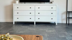A modern living room with a white TV stand, a flat-screen TV, a wooden coffee table, and two remote controls. - JUPAS° | Saartal Suite - Smart & Netflix (Konz)