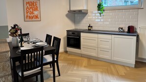 A modern kitchen with white cabinetry, a built-in oven, and a window overlooking a brick building. - JUPAS° | Saartal Suite - Smart & Netflix (Konz)
