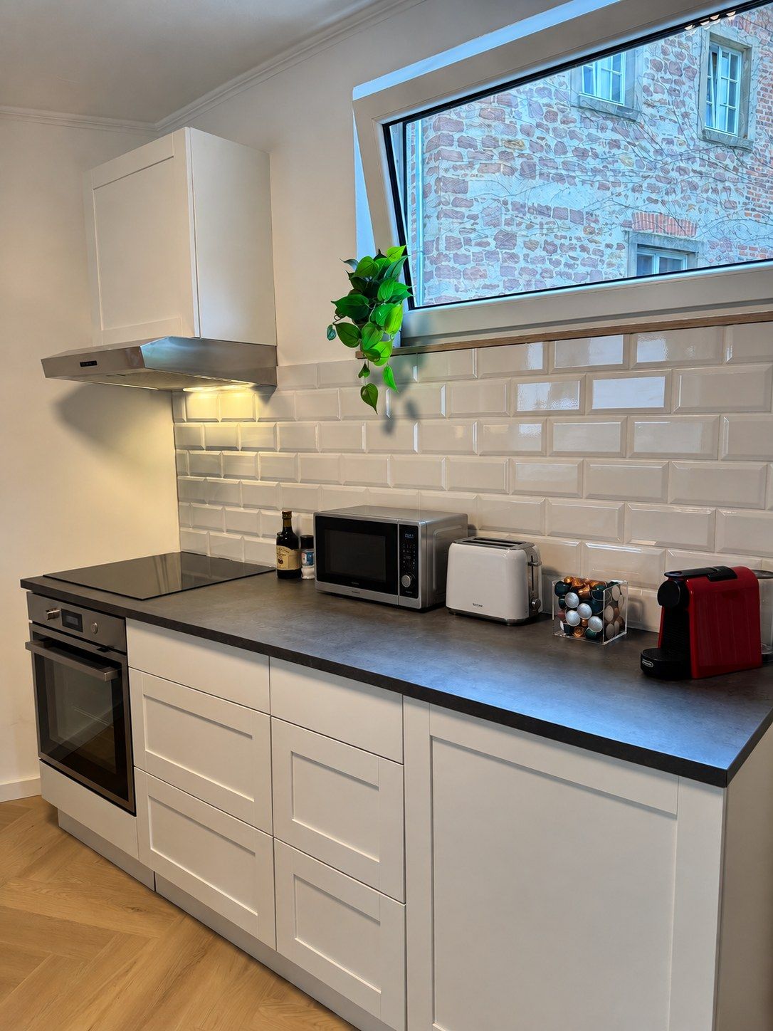 Eine moderne Küche mit weißen Schränken, einer schwarzen Arbeitsplatte, einer Mikrowelle, einem Toaster und einem Fenster mit Blick auf ein Backsteingebäude.