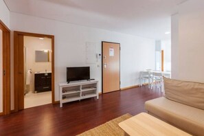 Ett modernt vardagsrum med en soffa, en tv på ett tv-bord, ett matbord med stolar och en dörr med en skylt.