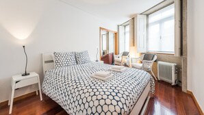 Ein Schlafzimmer mit Bett, Nachttisch, zwei Stühlen, Heizkörper und Fenster.