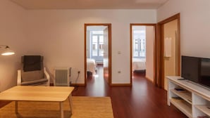 Ein modernes Wohnzimmer mit einer Couch, einem TV-Schrank und einer Heizung. Zwei Türen führen in andere Räume.