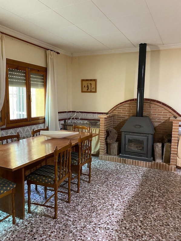 Un coin repas avec une table et des chaises en bois, une cheminée et une fenêtre avec des rideaux.