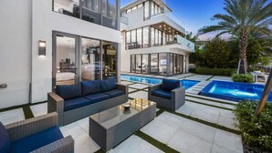 A modern two-story house with a large glass facade, a swimming pool, outdoor furniture, and a well-maintained garden.