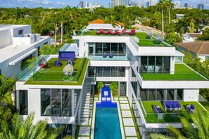 A modern multi-story house with a rooftop pool, multiple lounge areas, and a city skyline in the background.