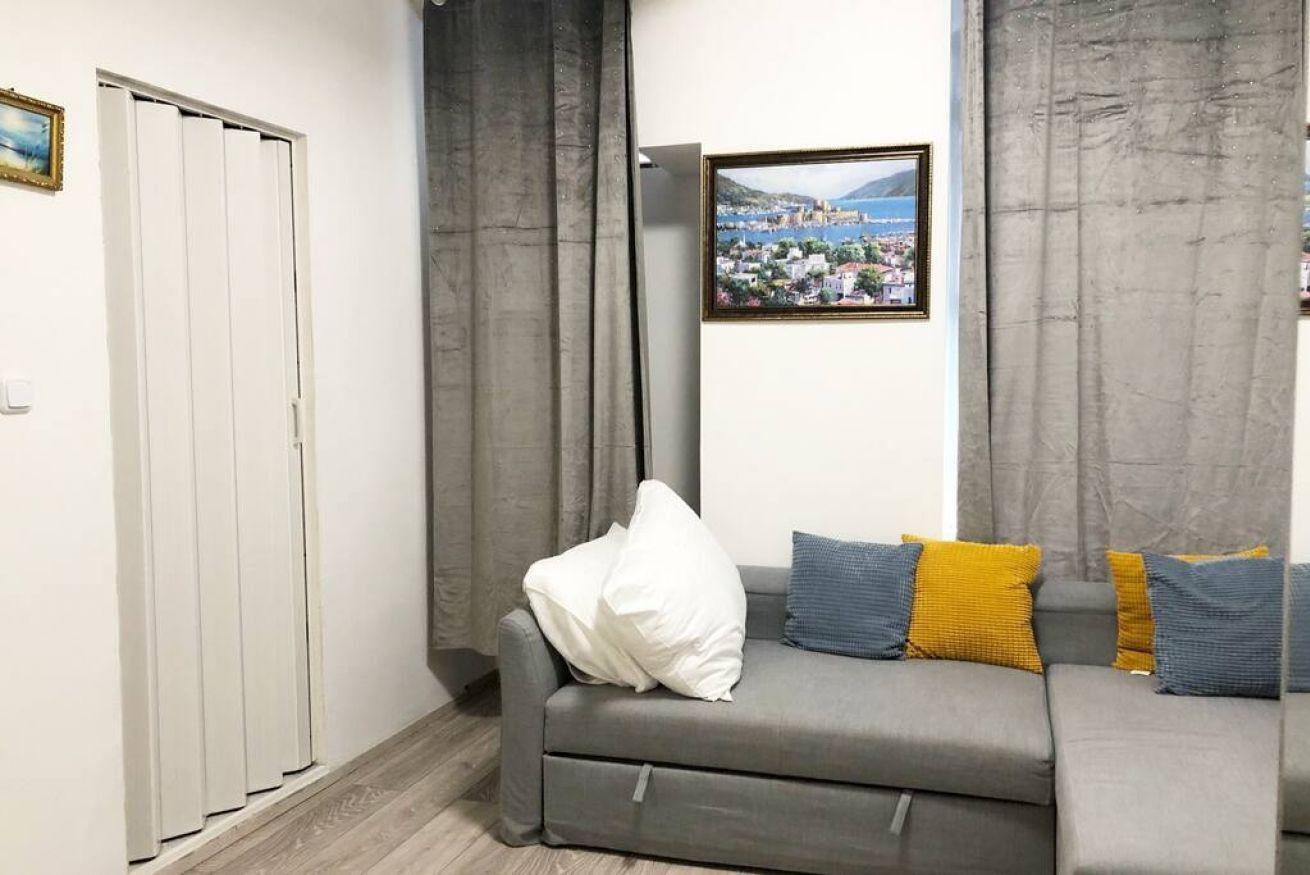 A living room with a grey sofa, a white pillow, and a framed picture on the wall.