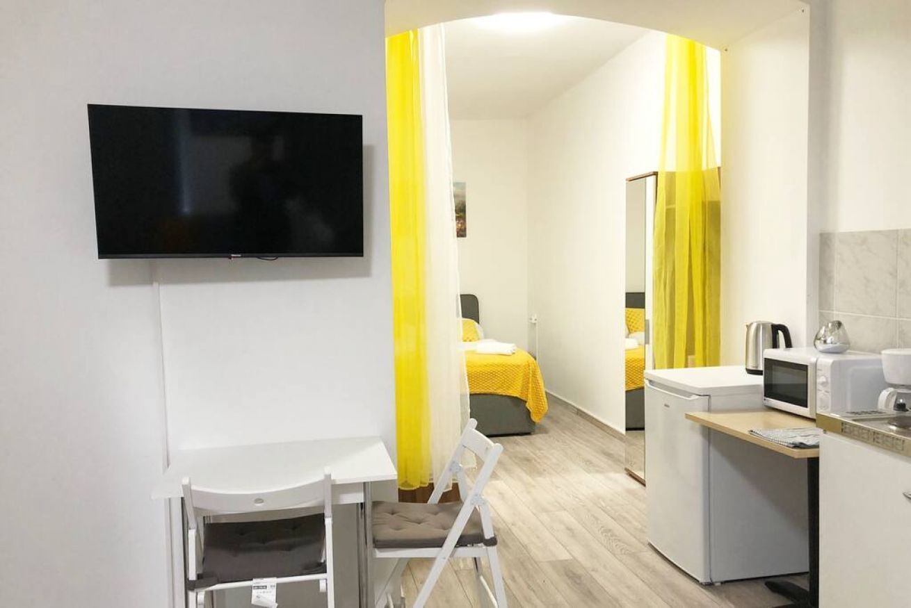 Camera d'albergo compatta con TV, angolo cottura, un letto con tende gialle e bagno con specchio.