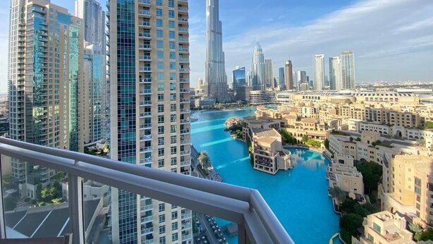 A high-rise building with a view of a cityscape, including a prominent skyscraper and a body of water. - Durrani Homes - The Residences 5BR Besides Dubai Mall with Burjkhalifa and Fountain view (Dubai)