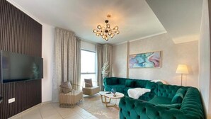 A modern living room with a teal sofa, a flat-screen TV, a chandelier, and a large window with curtains. - Durrani Homes - The Residences 5BR Besides Dubai Mall with Burjkhalifa and Fountain view (Dubai)