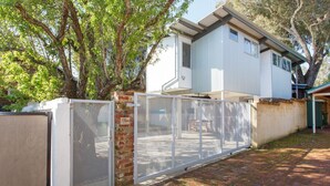 A two-story house with a fenced backyard, a brick wall, and a tree. - Drift Studio - Cosy Fremantle Hideaway (Beaconsfield)