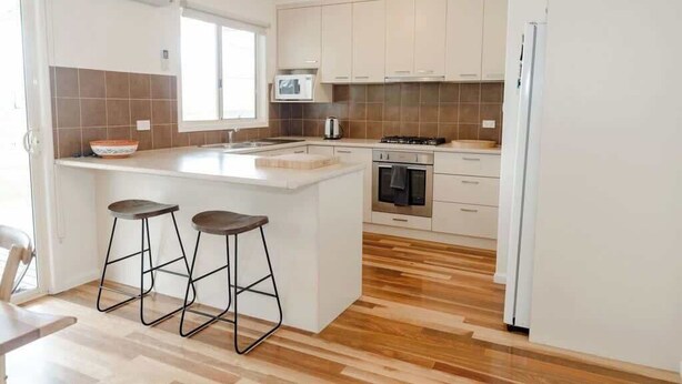 A modern kitchen with a central island, bar stools, a microwave, oven, and a refrigerator.