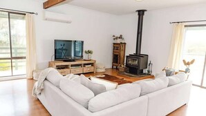 A modern living room with a white sofa, a TV, a wooden cabinet, and a wood-burning stove.