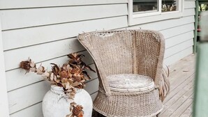 A wicker chair and a large vase with dried flowers on a wooden porch.