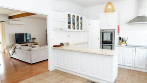 A modern kitchen with white cabinetry, a central island, and a dining area with a sofa and TV.