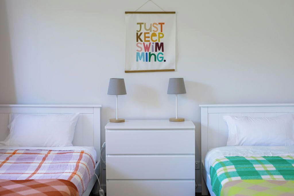 Una camera d'albergo con due letti, un comodino con lampade e un poster motivazionale appeso al muro.