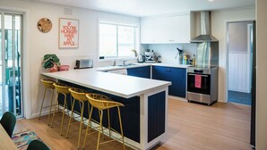 A modern kitchen with a central island, bar stools, a stainless steel oven, and a large window. - The Shark Haus Summar (Peterborough)
