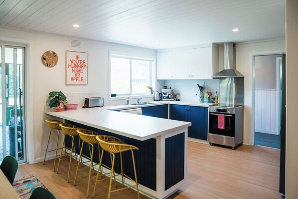A modern kitchen with a central island, bar stools, a stainless steel oven, and a large window.
