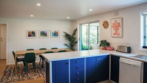 A modern kitchen with a central island, blue cabinets, and a dining area with green chairs. - The Shark Haus Summar (Peterborough)