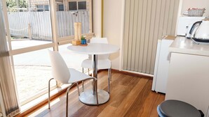 A kitchen with a round table, chairs, a trash bin, and a window with a view of a wooden fence.