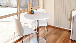 A room with a white table and chairs, a wooden floor, a sliding glass door, and a view of a building outside.