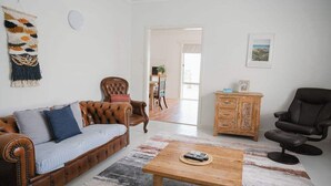 Un salon avec un canapé en cuir marron, une table basse en bois, un fauteuil en cuir noir, un meuble en bois et une décoration murale en macramé.