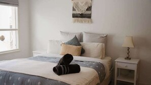 Une chambre à coucher avec un lit, des oreillers, une table de chevet, une lampe et un objet décoratif accroché au mur.