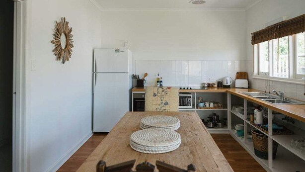 Une cuisine avec une table en bois, des placards blancs et un réfrigérateur.