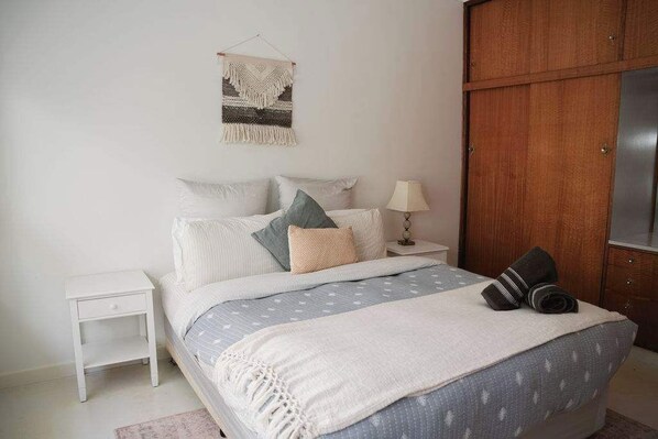 A bedroom with a bed, nightstand, lamp, and wardrobe. - Neptunes Guest House (Port Campbell)