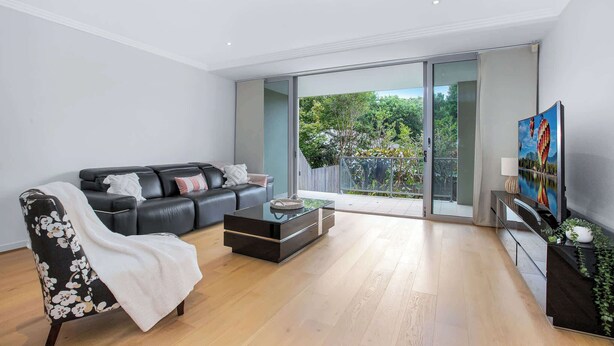 A modern living room with a black leather sofa, a floral armchair, a glass coffee table, and a TV on a black stand. - Wonderful Warrawee with Parking and backyard (Warrawee)