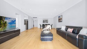 A modern living room with a flat-screen TV, a black leather sofa, a coffee table, and a dining area with chairs and a table. - Wonderful Warrawee with Parking and backyard (Warrawee)