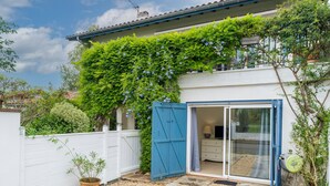 Een huis met een witte gevel, een blauwe deur en een tuin met bloempotten.