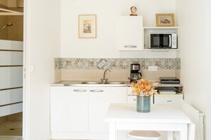A compact kitchen with a microwave, coffee maker, and a small table with a vase of flowers.