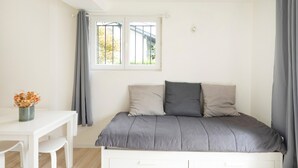 Een slaapkamer met een bed, een raam met gordijnen, een bureau met stoel en een vaas met bloemen.