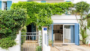 Een wit gebouw met een blauwe deur, een bord met nummer 5 en een tuin met een metalen hek.