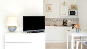 Een moderne keuken met witte kasten, een magnetron, een koffiezetapparaat en een flatscreen televisie op een witte standaard.