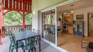 Un espace repas comprenant une table et des chaises, une porte-fenêtre coulissante donnant sur une cuisine, et une pergola rouge.
