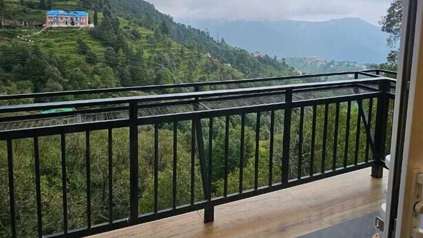 Un balcón con baranda metálica que da a un paisaje montañoso con campos en terrazas y una vista distante de una colina con una edificación.