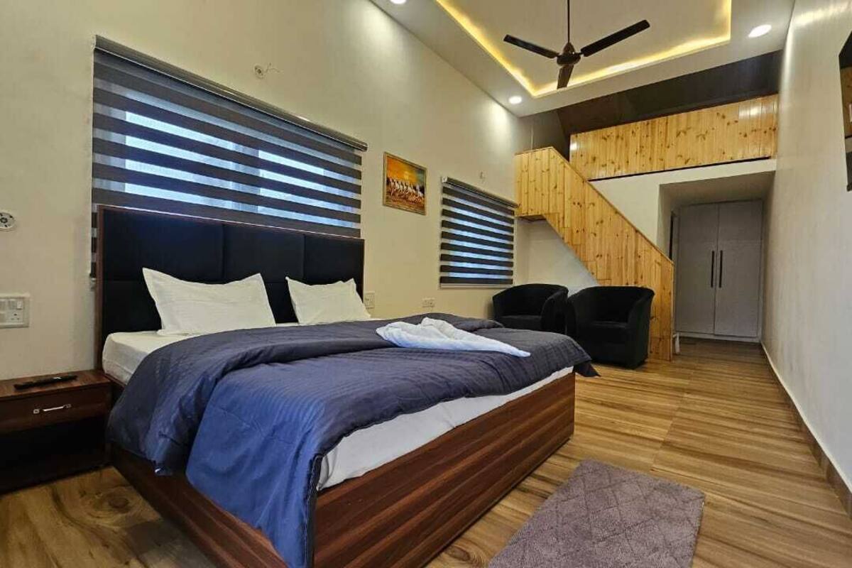 Quarto com cama, mesa de cabeceira e escada para um andar superior.